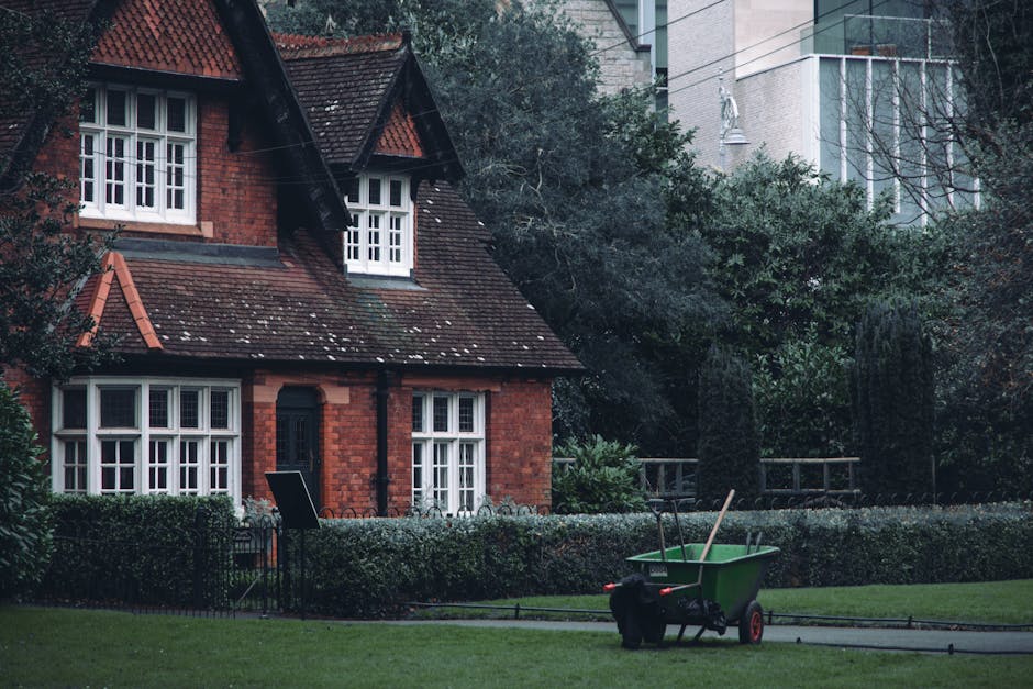Aerial black and white view of a residential neighborhood with closely packed houses featuring pitched roofs, surrounded by trees and garden spaces. The gardens have a mix of lawns, paved pathways, an